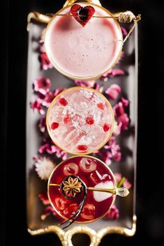 three different types of cocktails in glasses on a tray with flowers and petals around them