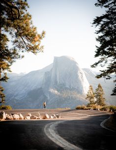 a man standing on the side of a road next to trees and mountain in the background