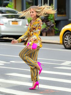 a woman in striped pants and heels is crossing the street with her hair blowing in the wind