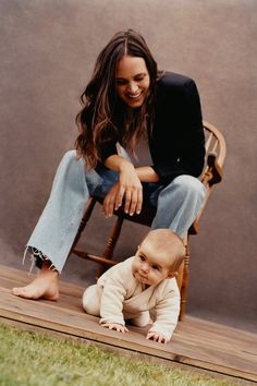 a woman sitting on top of a wooden chair next to a baby