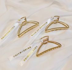 three pairs of gold colored metal clothes pins with white ribbons on them sitting on a white sheet