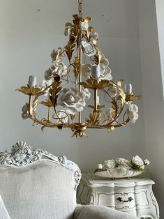 a chandelier hanging from the ceiling in a living room with white furniture and flowers