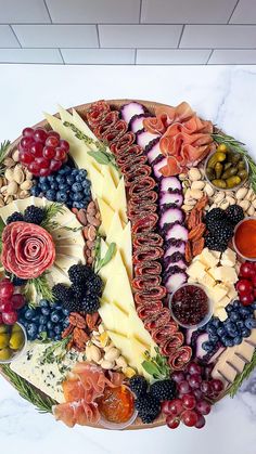 a platter filled with different types of cheeses and fruit on top of a marble counter