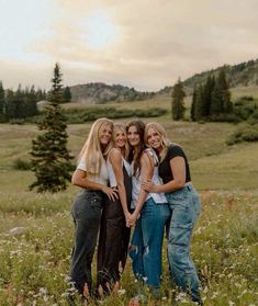 four women standing together in a field with mountains in the background