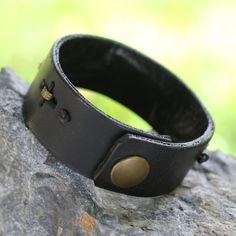 Men's ruggedly handsome black leather bracelet by Gill Quarcoopome. The masculine bracelet is adorned with a clever arrangement of crimped antique brass inserts which have been hand-stitched with leather cords creating a discreet contrast of powerful elegance. Leather Brass Inserts Snap clasp Avoid contact with water Handmade in & fairly traded from Ghana Steampunk Leather Bracelet As A Gift, Steampunk Leather Bracelet Perfect As A Gift, Adjustable Leather Wristband With Waxed Finish, Rugged Leather Bracelets, Classic Adjustable Leather Bracelet With Waxed Finish, Masculine Leather Bracelet, Masculine Adjustable Leather Bracelet, Masculine Adjustable Leather Bracelet For Everyday, Vintage Leather Jewelry With Waxed Finish