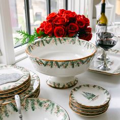 red roses are sitting in a bowl on a table next to plates and wine glasses