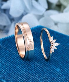 two gold wedding rings with flowers on each side, sitting next to each other in front of a blue towel