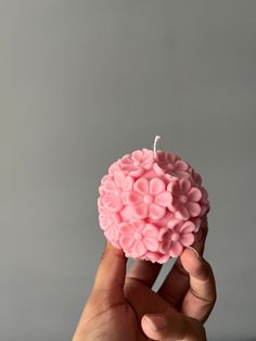 a hand holding a small pink candle with flowers on it's top, in front of a gray background