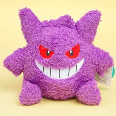 a purple stuffed animal with big red eyes and fangs on it's face, sitting in front of a yellow background