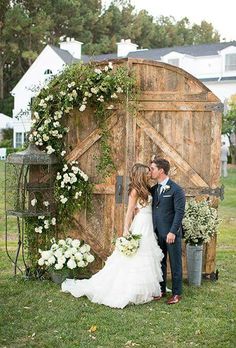 a man and woman are kissing in front of a wooden structure with flowers on it