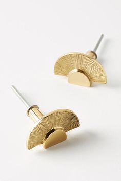 two pairs of gold earrings on a white surface, one has a circular design and the other has a curved shape