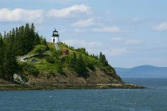 a light house sitting on top of a lush green hillside next to the ocean and trees