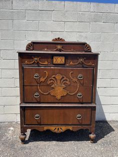 an old wooden dresser with ornate carvings on the top and bottom drawers, in front of a brick wall