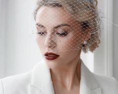 a woman wearing a white suit with a birdcage veil on her head and red lips