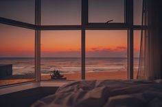 a bed sitting in front of a window next to the ocean at sunset or dawn