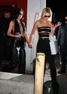 two women in black and white outfits are walking down the street with one holding her hand out