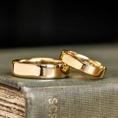 two gold wedding rings sitting on top of an old book