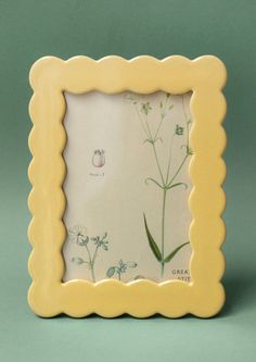 a small yellow frame with flowers and leaves on the inside is shown in front of a green background