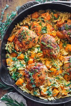 a skillet filled with chicken, pasta and carrots on top of a wooden table