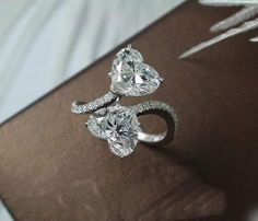 two pear shaped diamond rings sitting on top of an open book with feathers flying in the background