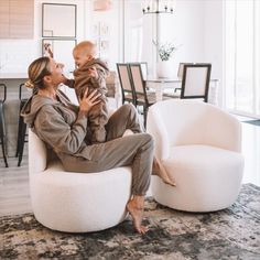 a woman holding a baby while sitting on top of a white chair in a living room