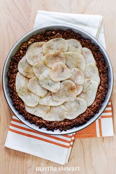 a pie with sliced bananas in it on top of a wooden table next to an orange and white towel