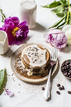 a plate topped with pancakes covered in frosting next to coffee beans and flowers on a table