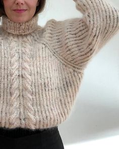 a woman is wearing a sweater and posing with her hands on her head while looking at the camera