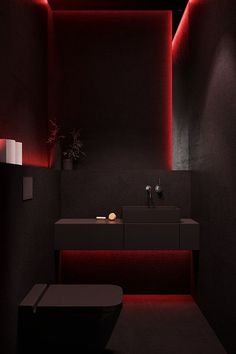 a black bathroom with red lighting on the walls and countertop, along with a toilet