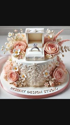 a wedding cake decorated with pink roses and an engagement ring sits on top of it