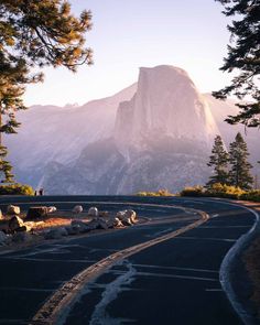 an empty road in front of a mountain with trees and rocks on both sides, at sunset