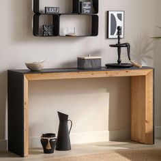 a wooden table topped with black vases next to a wall mounted shelf filled with pictures