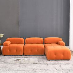 an orange couch sitting on top of a white rug next to a vase with flowers