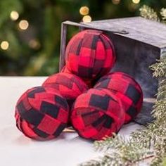 four red and black buffalo plaid balls sitting in front of a christmas tree