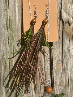 two necklaces with feathers and beads hanging on a piece of wood next to a card