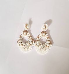 "Boho White and Gold Raffia embellished statement medium size earrings. The earring is hand embroidered using various elements like Raffia, handmade silk pompoms, faux pearl, glass beads, and much more material. This lightweight medium size Raffia white with gold accent earring is a piece of perfect wedding jewelry. The Earrings measure about approx. 2.75\" long and 2.10\" wide. PS: Carnation jewelry is handmade & handcrafted in India hence there is a possibility of a slight or small imperfe Elegant Gold Tassel Earrings For Beach, Elegant Summer Chandelier Earrings With Tassels, Elegant Tassel Earrings For Beach In Summer, Elegant Summer Tassel Chandelier Earrings, Elegant Summer Tassel Earrings For Beach, White Dangle Tassel Earrings For Party, White Tassel Chandelier Drop Earrings, White Tassel Earrings For Party, Bohemian White Earrings For Beach