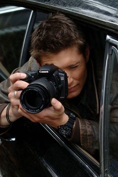 a man holding a camera in his hand while looking out the side window of a car