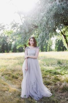 a woman in a dress standing under a tree with her arms crossed and looking at the camera