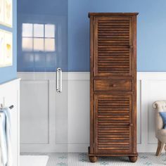 a tall wooden cabinet sitting next to a chair in a blue and white bathroom with tile flooring