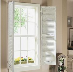 an open window with white shutters in a living room