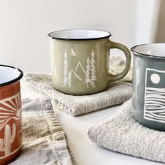 two mugs sitting on top of a towel next to each other