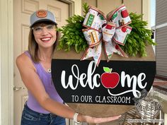 a woman holding up a welcome sign with an apple on it and the words welcome to our classroom