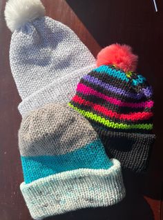 two knitted hats sitting on top of a wooden table next to eachother