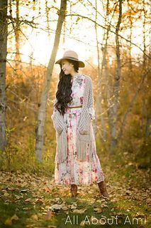 a woman standing in the woods wearing a dress and hat