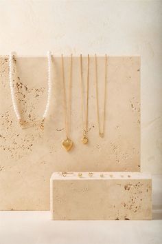 three necklaces are hanging on the wall next to a box with pearls and gold heart pendants