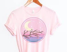 "The Cherry Blossom Sunset Vaporwave T-shirt is perfect for anyone who wants to add a touch of kawaii to their wardrobe. The shirt is made of soft, combed cotton and polyester for a comfortable fit. It's machine-washable and resistant to fading, making it a great choice for everyday wear. The shirt features a beautiful cherry blossom print in shades of pink, purple, and blue. It's perfect for anyone who loves Japanese fashion or lofi vibes. * Unisex * Premium & Soft * Combed & Ringspun Cotton/Po Kawaii Tshirt, Kawaii T Shirt, Spring Harajuku T-shirt With Funny Print, Harajuku Style Funny Print T-shirt For Spring, Aesthetic Graphic Print Tops For Spring, Spring Kawaii Shirt With Graphic Print, Spring Aesthetic Graphic Print T-shirt, Spring Aesthetic Graphic T-shirt, Spring Moon Print Cotton T-shirt