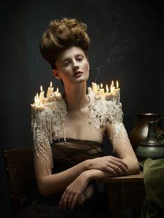 a woman sitting in front of a table with candles on top of her head and arms