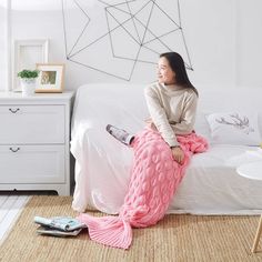 a woman sitting on top of a bed next to a pink mermaid tail shaped blanket