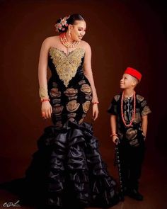 a woman in a black dress standing next to a little boy wearing a red hat