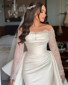 a woman wearing a wedding dress with long sleeves and a veil on her head is posing for the camera